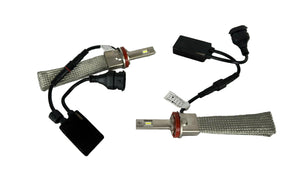 Two car headlight bulbs with wiring on a white tiled floor.