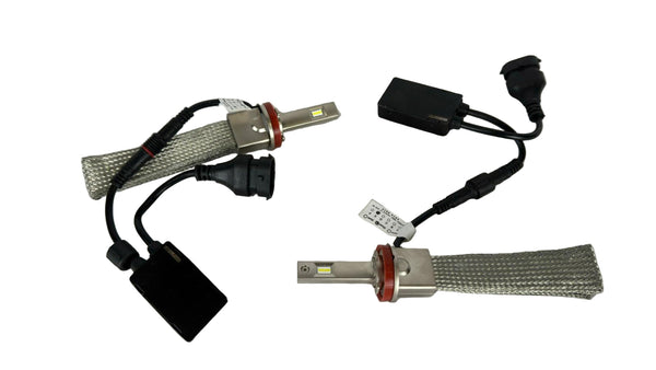 Two car headlight bulbs with wiring on a white tiled floor.